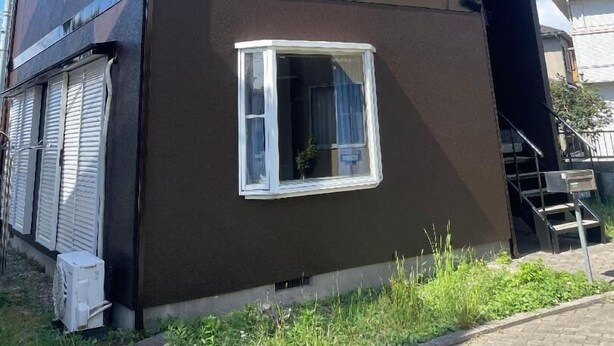 Ein zweigeschossiges Gebäude mit dunkler Fassade, weißen Fensterrahmen und einer sichtbaren Treppe, die zu der oberen Etage führt.