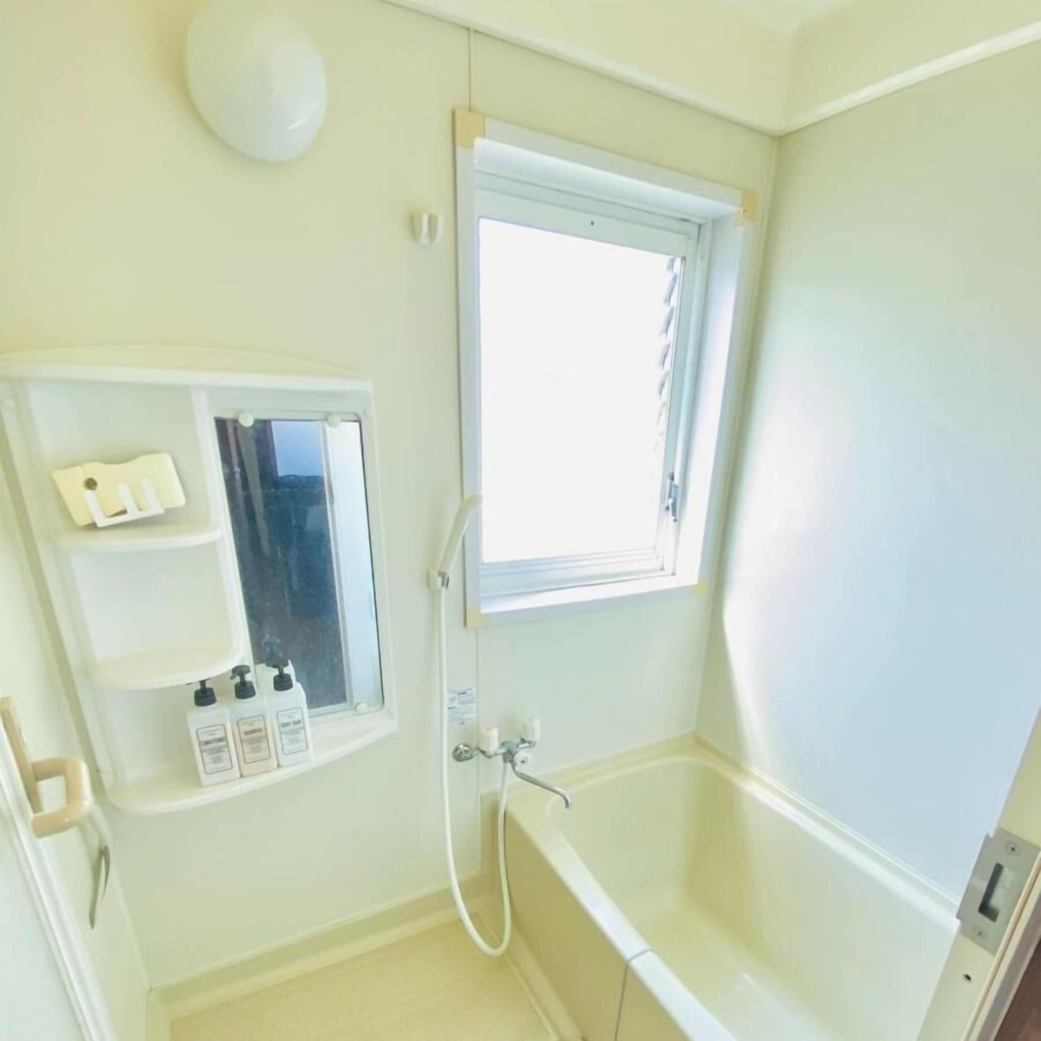 Ein Badezimmer mit einer Badewanne, einem Fenster, einem Spiegel und einem Ablagefach mit Toilettenartikeln.