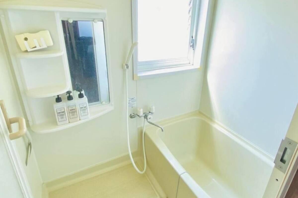 Ein Badezimmer mit einer Badewanne, einem Fenster, einem Spiegel und einem Ablagefach mit Toilettenartikeln.