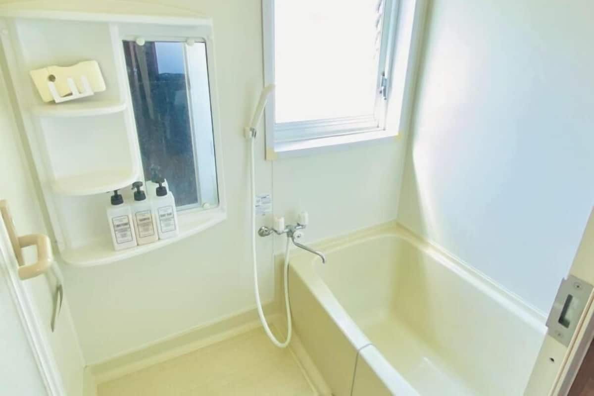 Ein Badezimmer mit einer Badewanne, einem Fenster, einem Spiegel und einem Ablagefach mit Toilettenartikeln.