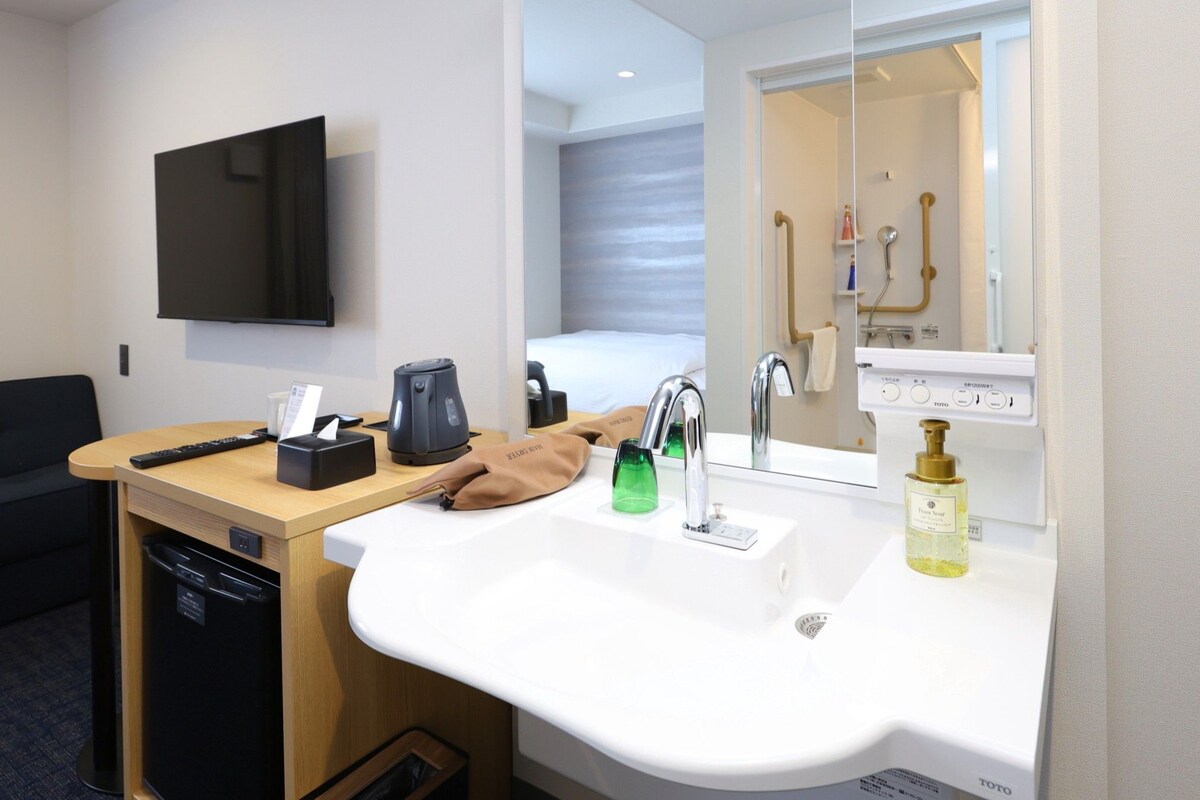 A hotel bathroom with a sink, mirror, and a television mounted on the wall.