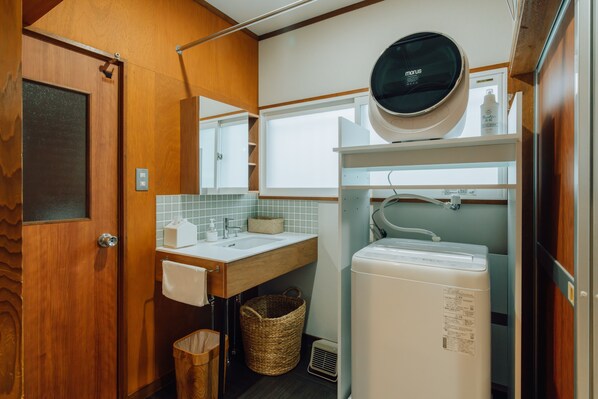 Une petite salle de bain avec une porte en bois, un lavabo blanc, un miroir, un radiateur blanc et une petite fenêtre.