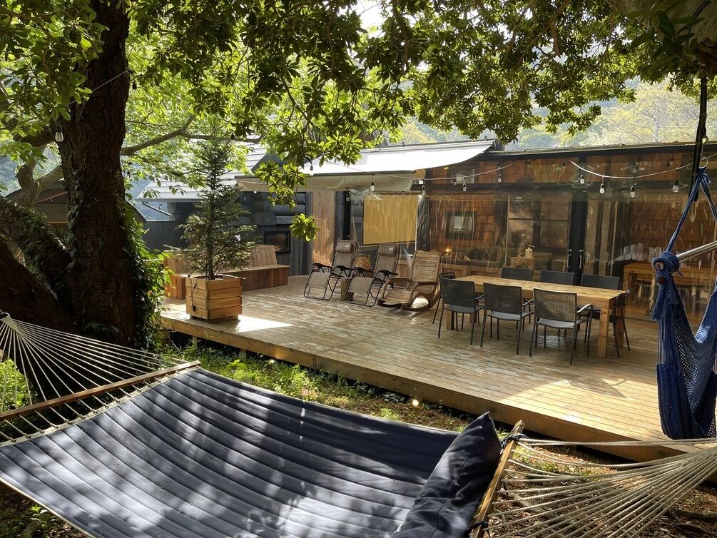 Um deck de madeira com móveis de exterior, uma rede e um vaso de planta.