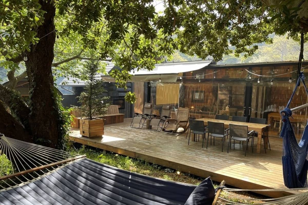Una terraza de madera con mobiliario exterior, una hamaca y una planta en maceta.