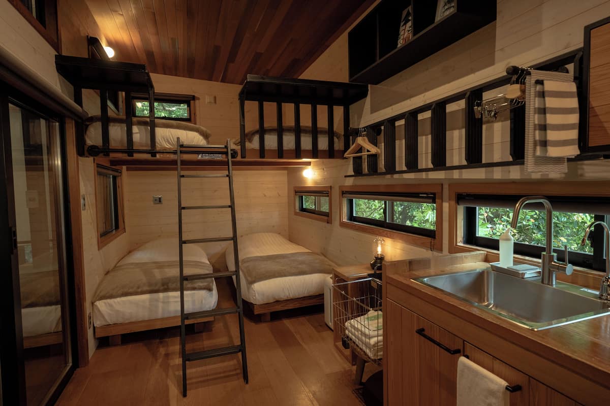 Una cabaña pequeña con literas, kitchenette y ventana con vista a la vegetación.