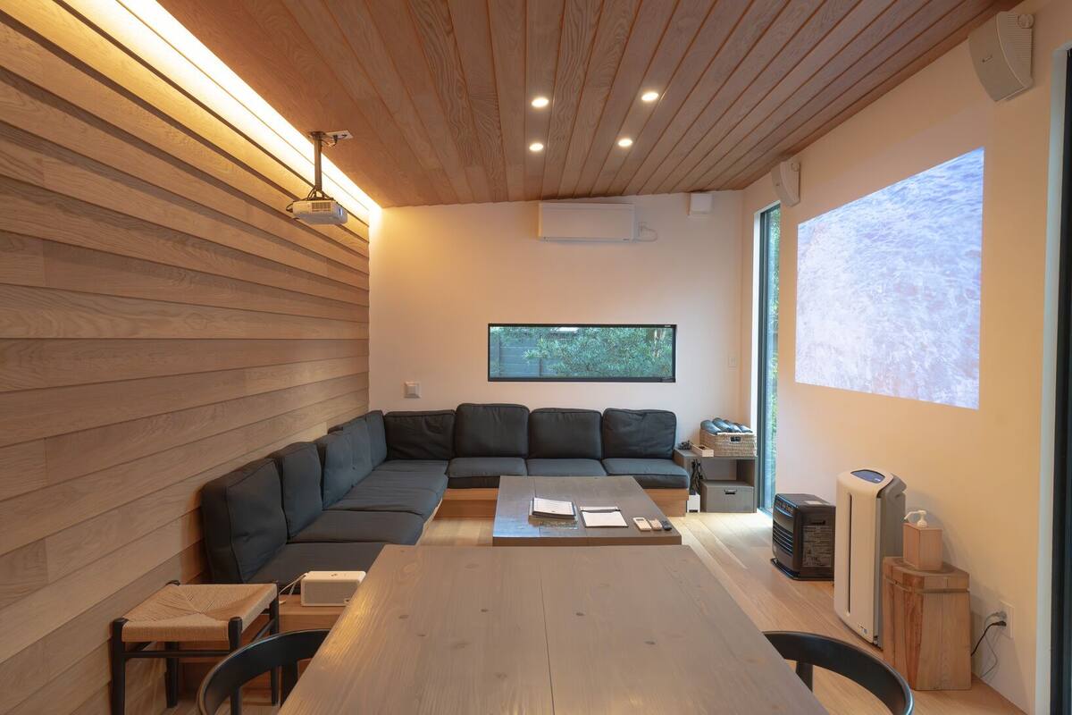 Un interior moderno con techo de madera, un sofá modular, una mesa de comedor y un ventanal grande.