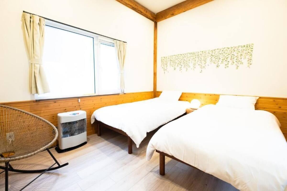Quarto com duas camas, uma cadeira de vime e uma janela com cortinas.