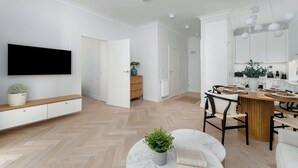 En moderne stue med et fladskærms-tv, en træbænk, et spisebord med stole og en potteplante.