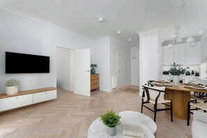 Ein modernes Wohnzimmer mit Flachbildfernseher, einer Holzbank, einem Esstisch mit Stühlen und einer Topfpflanze.
