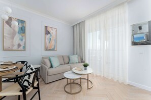 Ein modernes Wohnzimmer mit einer Couch, einem Esstisch mit Stühlen, einem kleinen runden Tisch mit einer Pflanze und Kunstwerken an den Wänden.
