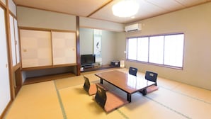 A traditional Japanese room with tatami flooring, a low table, chairs, a television, and a large window.