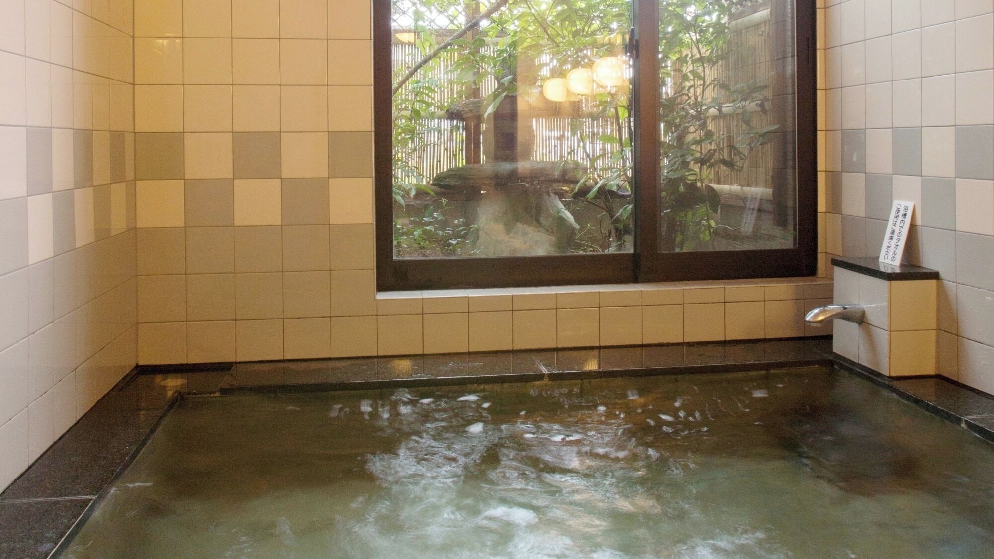 Un baño con bañera, paredes de azulejos y una ventana con vistas a la vegetación.