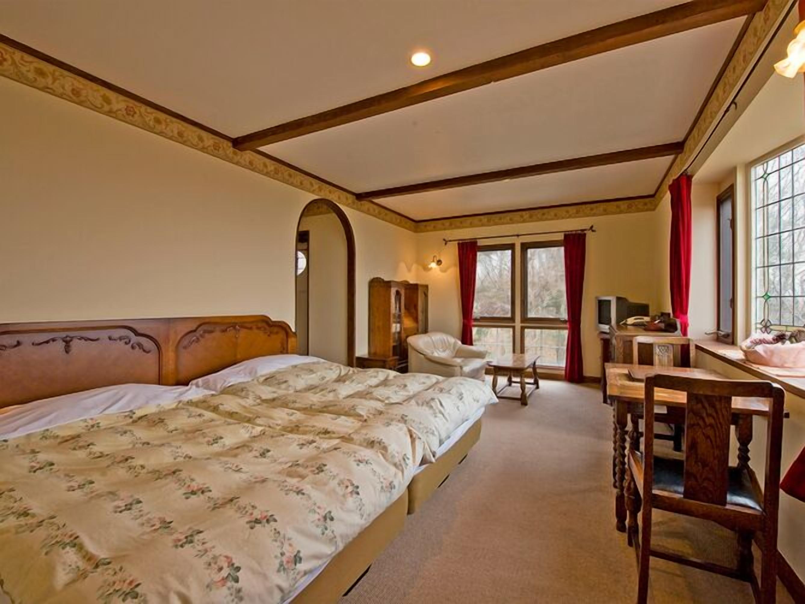A bedroom with a large bed, a desk, a chair, and a window with curtains.