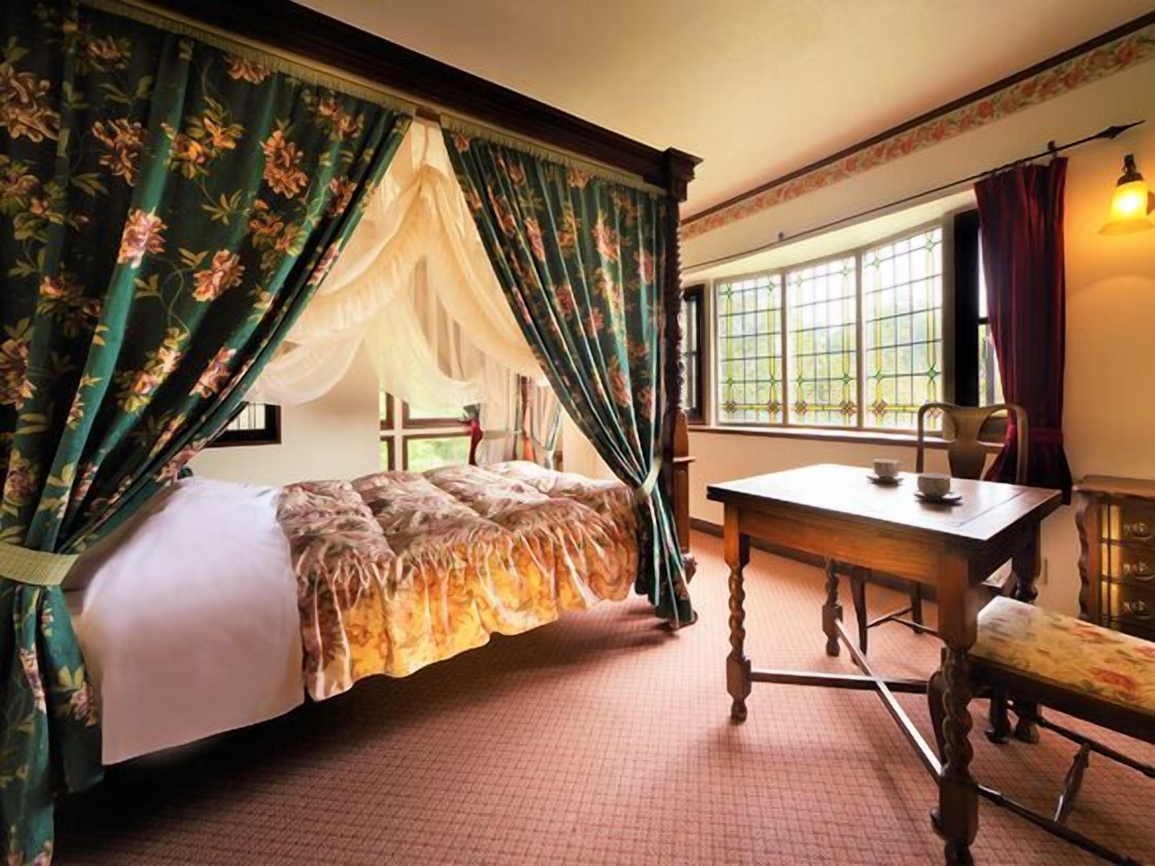 A room with a four-poster bed, a wooden desk, and a window with curtains.