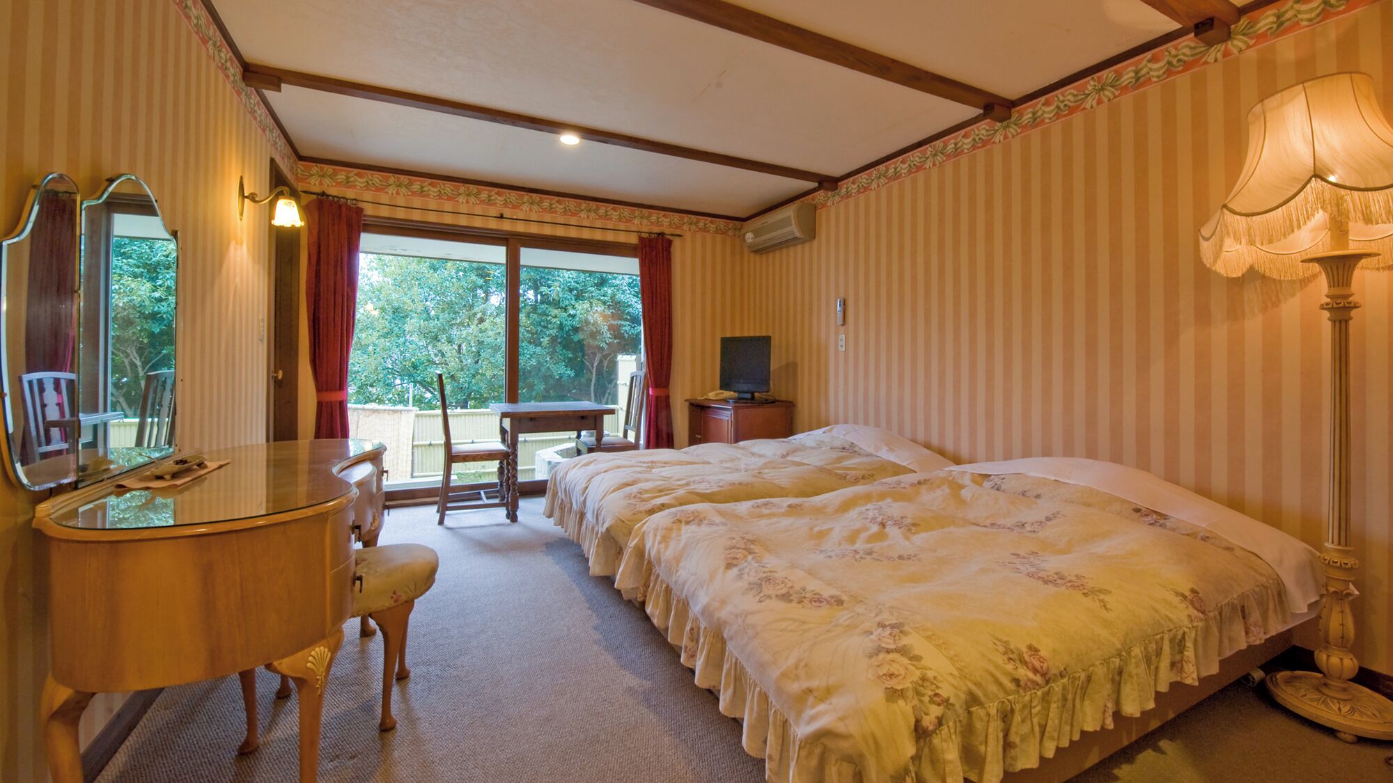 Habitación de hotel con cama, escritorio, silla, televisor y ventana con cortinas.