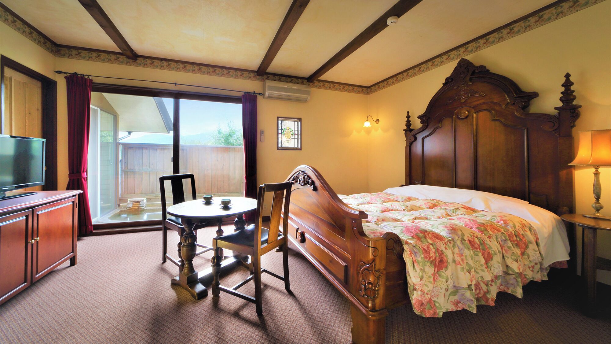 Habitación de hotel con cama, televisión, mesa y sillas, y vista al exterior.