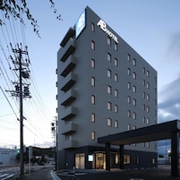 A multi-story hotel with a prominent 'AB HOTEL' sign, a covered entrance, and a parking area.