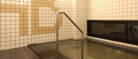 A tiled bathroom with a glass shower enclosure and a metal handrail.