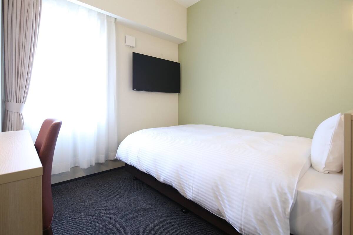 A hotel room with a bed, a desk, and a flat-screen TV mounted on the wall.