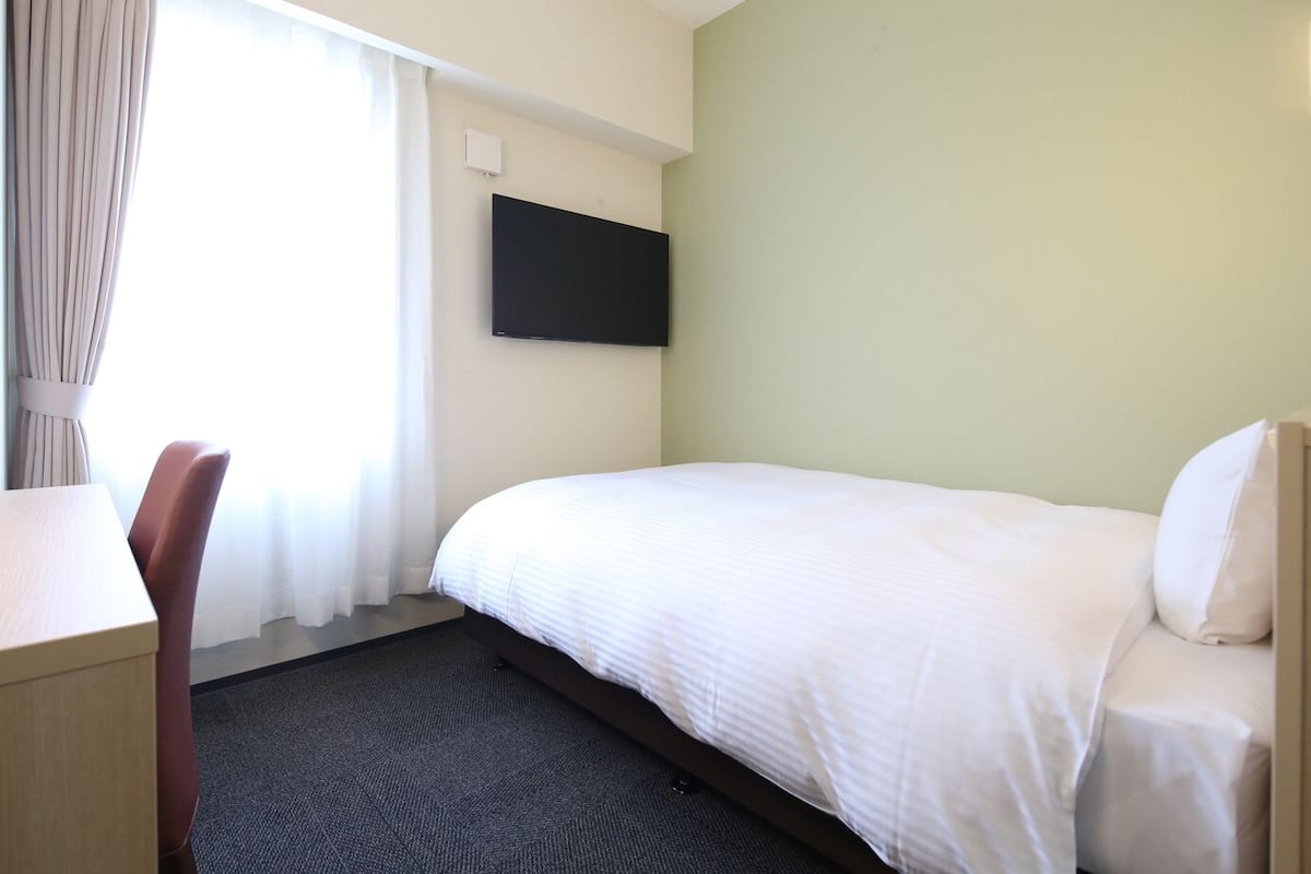 A hotel room with a bed, a desk, and a flat-screen TV mounted on the wall.
