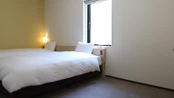 A hotel room with a single bed, a nightstand with a lamp, a window, and a wall-mounted control panel.