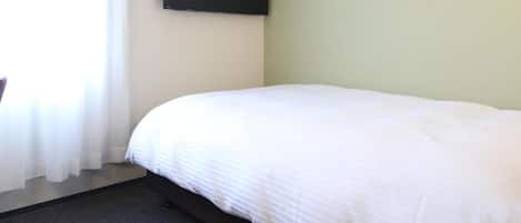 A hotel room with a bed, a flat-screen TV mounted on the wall, and a window with curtains.