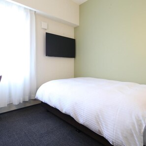 Ένα δωμάτιο ξενοδοχείου με ένα κρεβάτι, μια τηλεόραση επίπεδης οθόνης τοποθετημένη στον τοίχο και ένα παράθυρο με κουρτίνες.