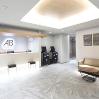 Un área de recepción de hotel con diseño moderno, que incluye un mostrador de recepción, dos cajeros automáticos negros, un sofá y un techo con tragaluz.