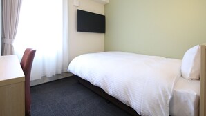 Une chambre d’hôtel équipée d’un lit, d’un bureau, d’une chaise, d’un téléviseur à écran plat fixé au mur et d’une fenêtre avec des rideaux.