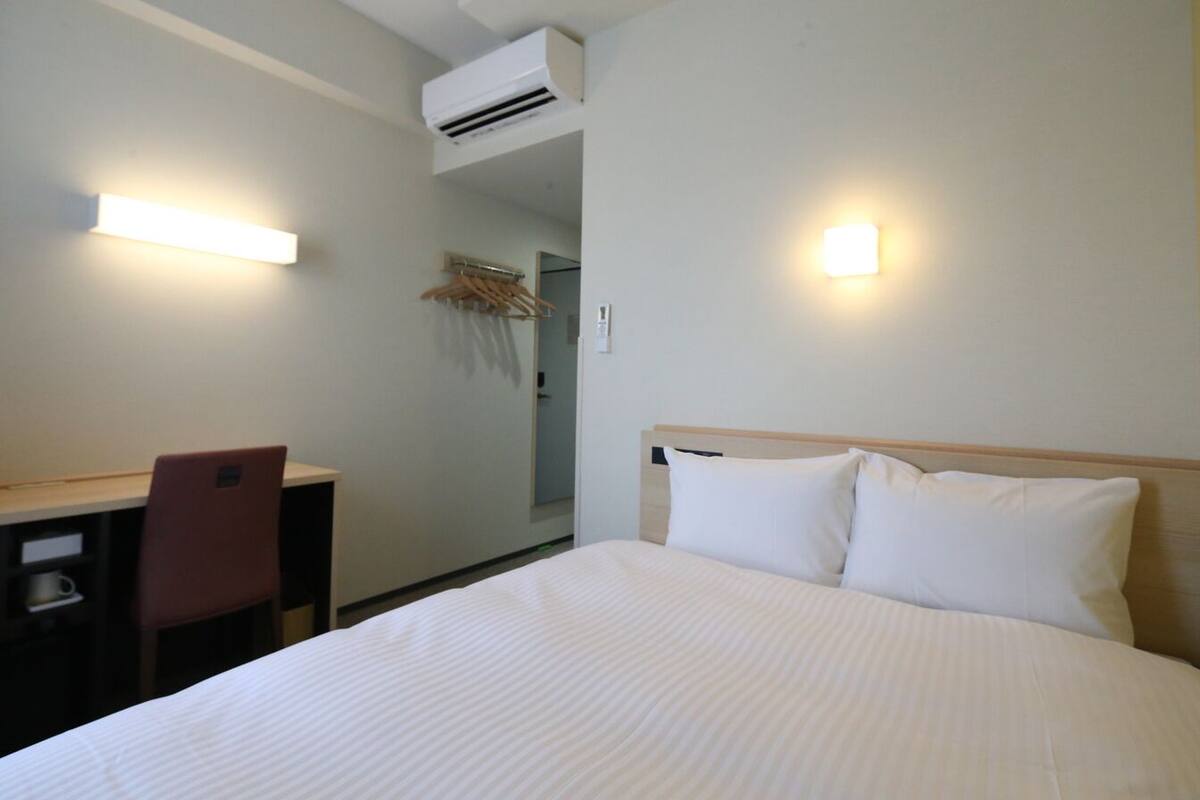 A hotel room with a bed, a desk, a chair, and two wall-mounted lights.
