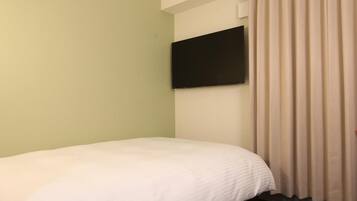A hotel room with a single bed, a flat-screen TV mounted on the wall, and a window with curtains.