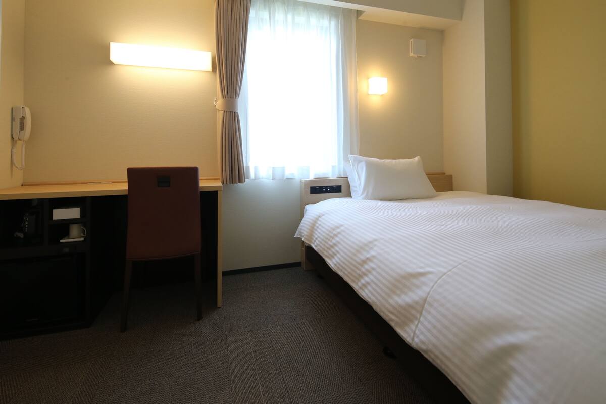 A hotel room with a bed, desk, chair, and a telephone.
