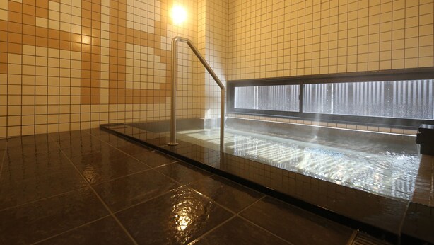 Une salle de bain carrelée avec une douche en verre et une barre d’appui en métal.