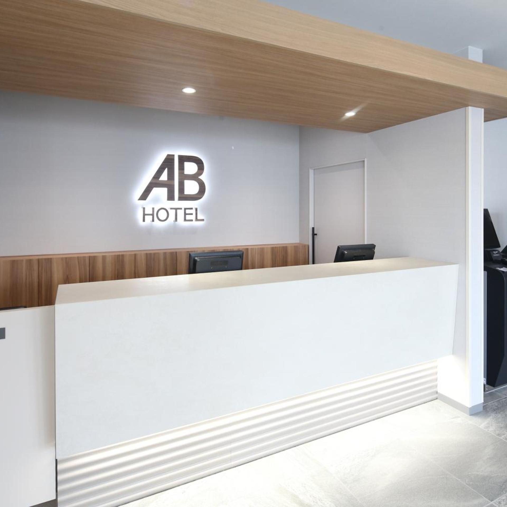 A hotel reception desk with a modern design, a wooden accent wall, and a logo above the desk.