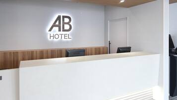 A hotel reception desk with a modern design, a wooden accent wall, and a logo above the desk.
