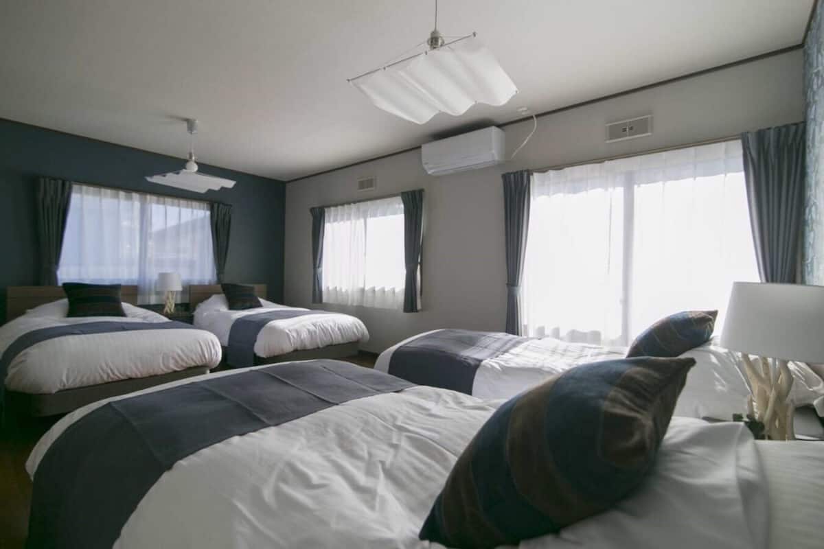 Ein Hotelzimmer mit zwei Betten, Deckenventilator, Klimaanlage und großen Fenstern mit Vorhängen.