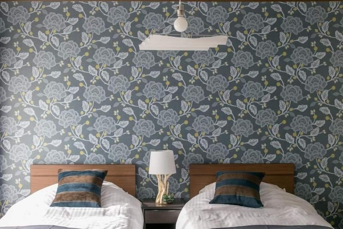 Ein Zimmer mit zwei Betten, einem Nachttisch mit Lampe und floralem Wandpapier.
