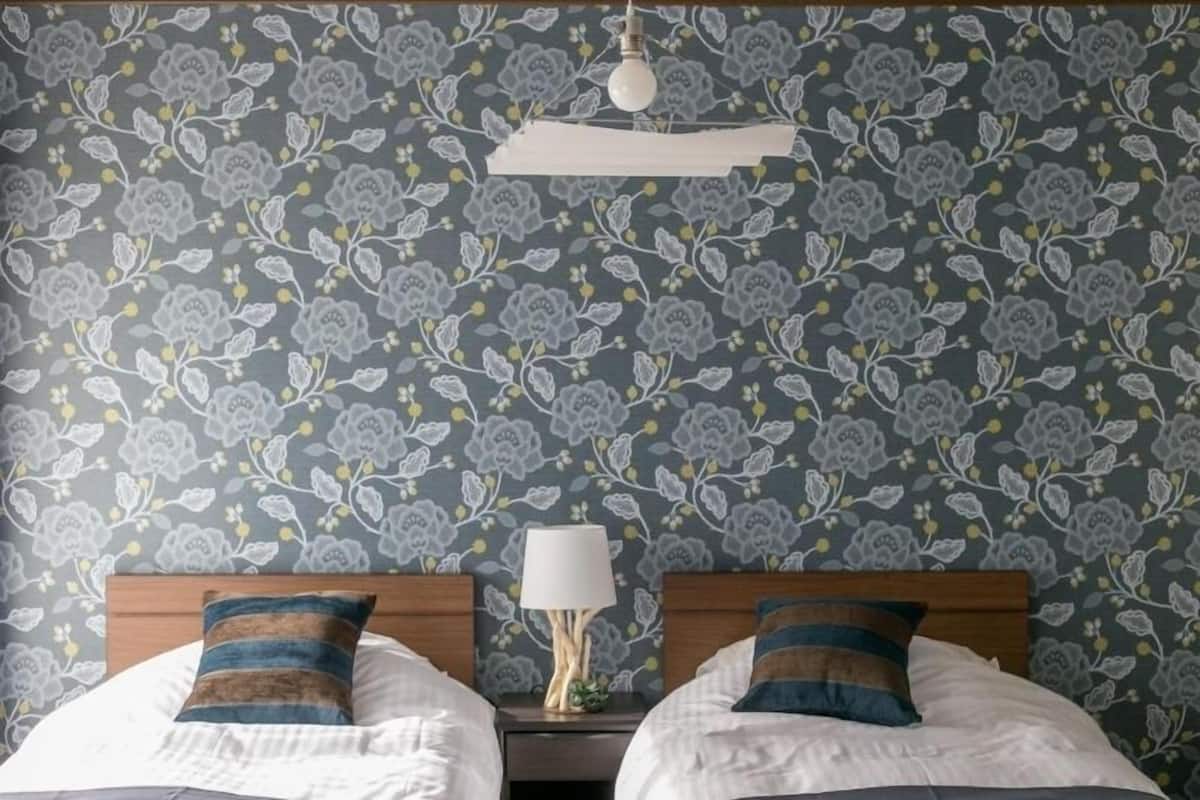 Ein Zimmer mit zwei Betten, einem Nachttisch mit Lampe und einem blumigen Wandbehang.
