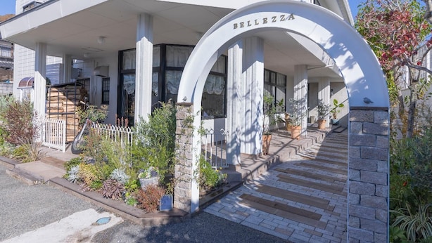 Un edificio con fachada blanca, un acceso cubierto y un cartel que dice 'BELLEZZA'.