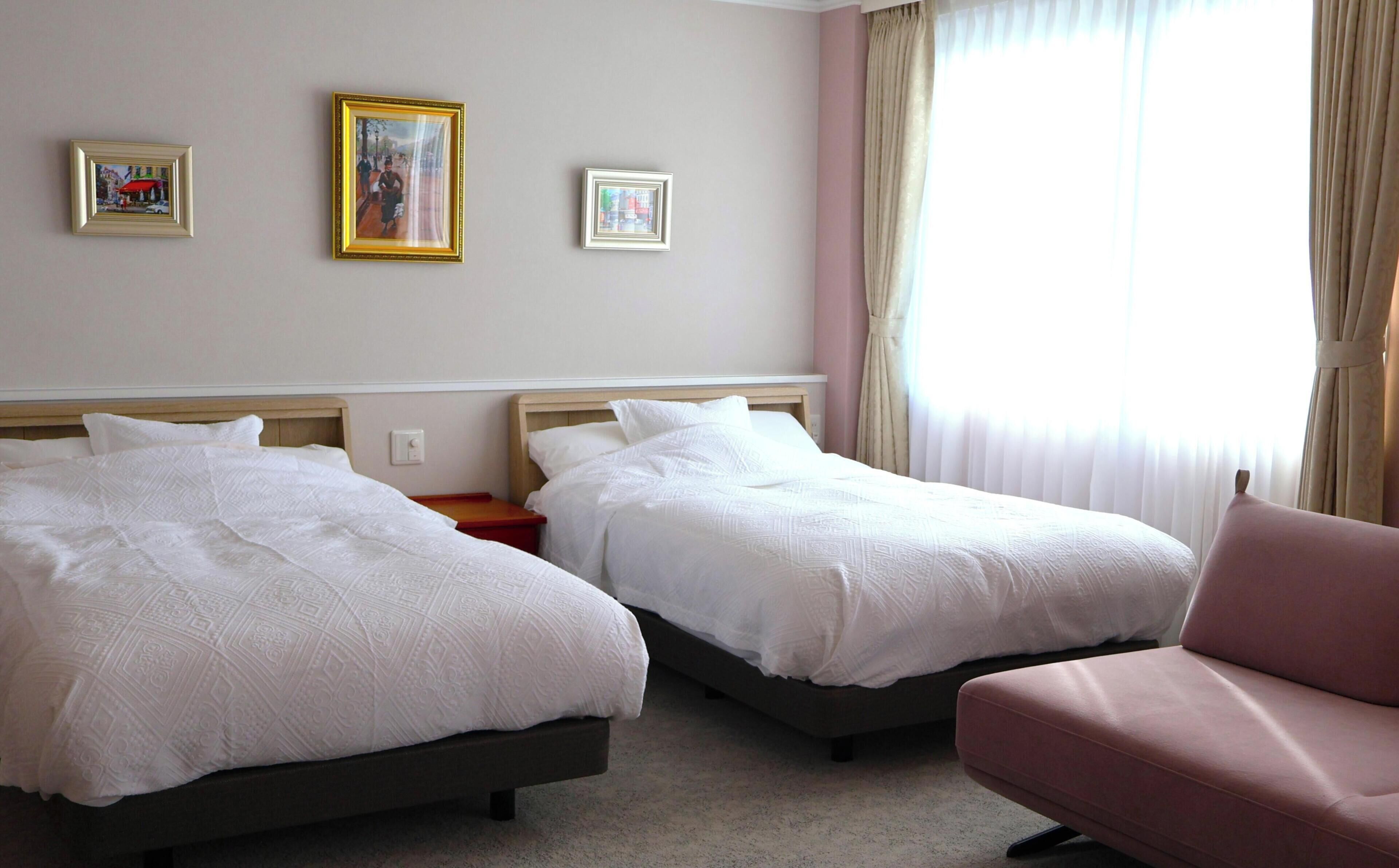 Habitación de hotel con dos camas, una silla y dos cuadros en la pared.