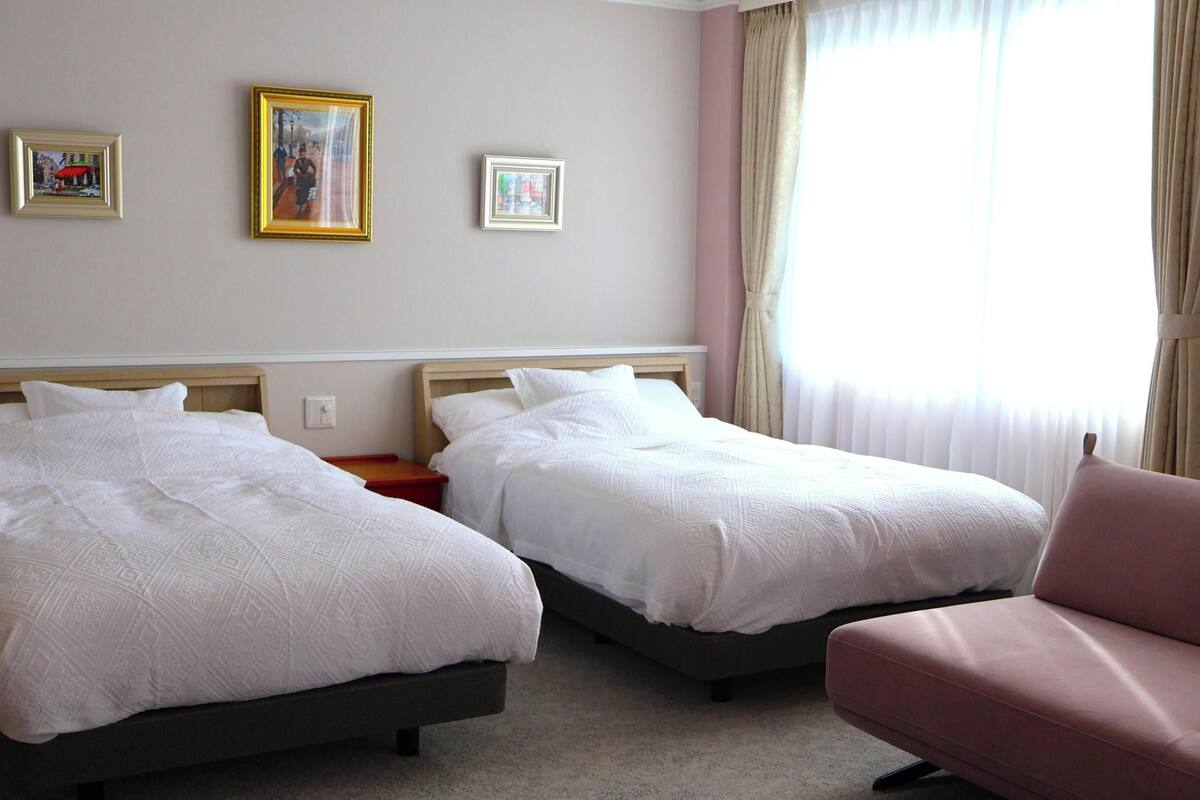 A hotel room with two beds, a chair, and two framed pictures on the wall.