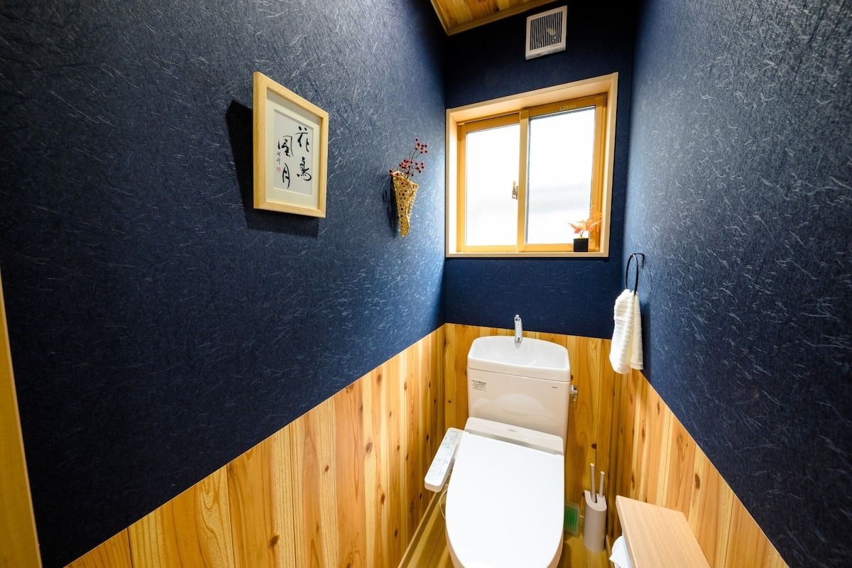 Une salle de bain avec un meuble-lavabo en bois, des toilettes, un lavabo, un tableau encadré et une fenêtre.