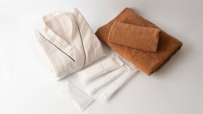 A neatly folded white bathrobe, a brown towel, and several white toiletry packets on a white surface. - Hotel R9 The Yard Tomioka Nanokaichi (Mooka)
