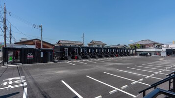 Un estacionamiento con una fila de habitaciones modulares, una parada de autobús y un edificio con señalización.