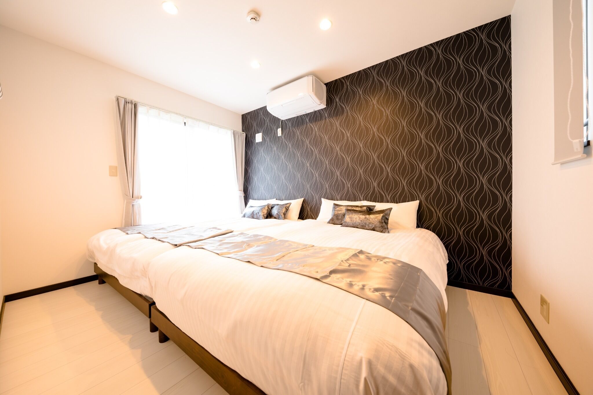A modern hotel room with a large bed, a patterned wall, and an air conditioning unit.