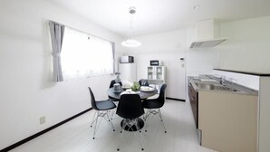 Una cuina moderna amb zona de menjador, parets blanques i una finestra amb cortines.