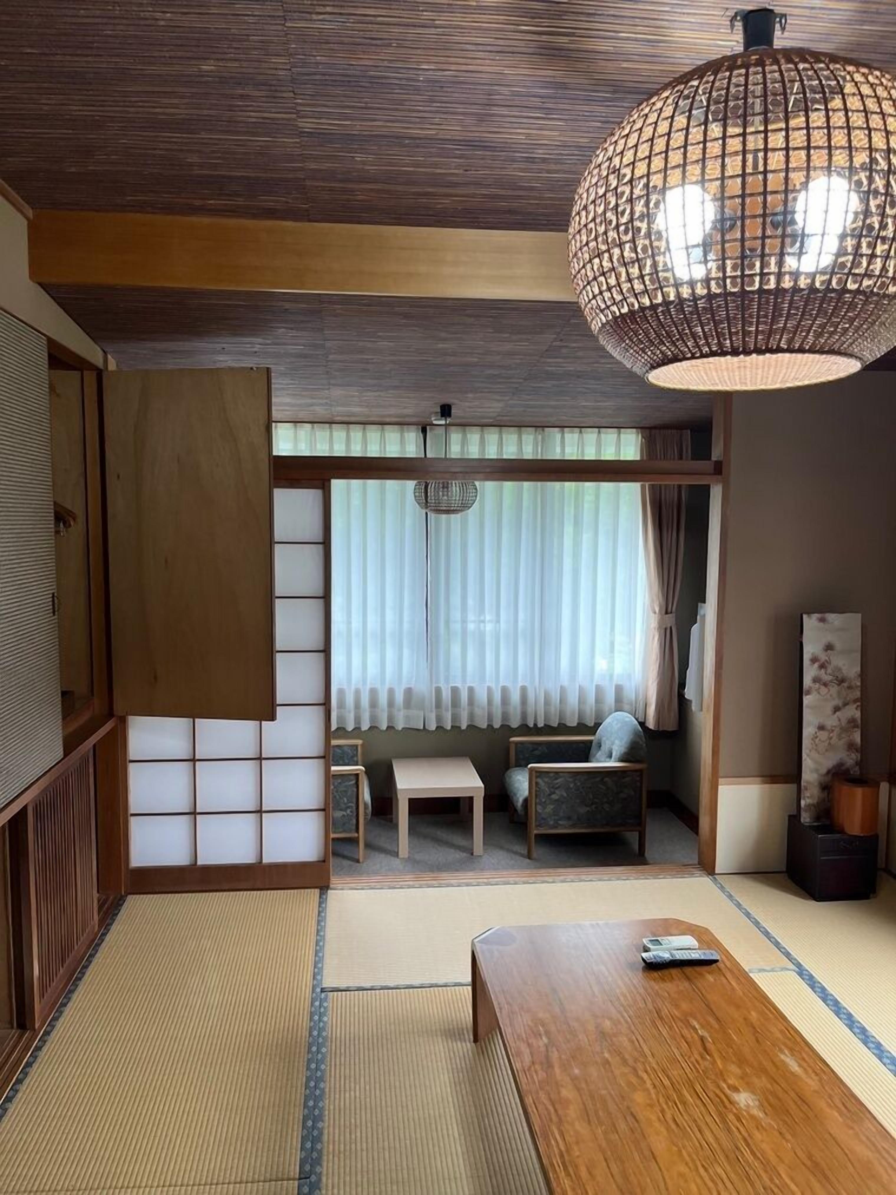 Ein traditioneller japanischer Raum mit Tatami-Boden, einem niedrigen Holztisch, einer Couch, einer Pendelleuchte und einer Schiebetür.