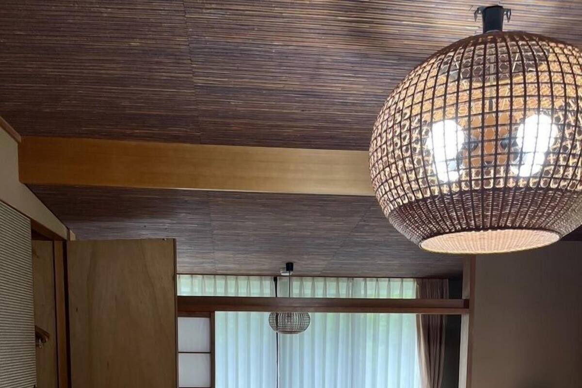 Una habitación japonesa tradicional con suelo de tatami, una mesa de madera baja, un sofá, una lámpara colgante y una puerta corredera.