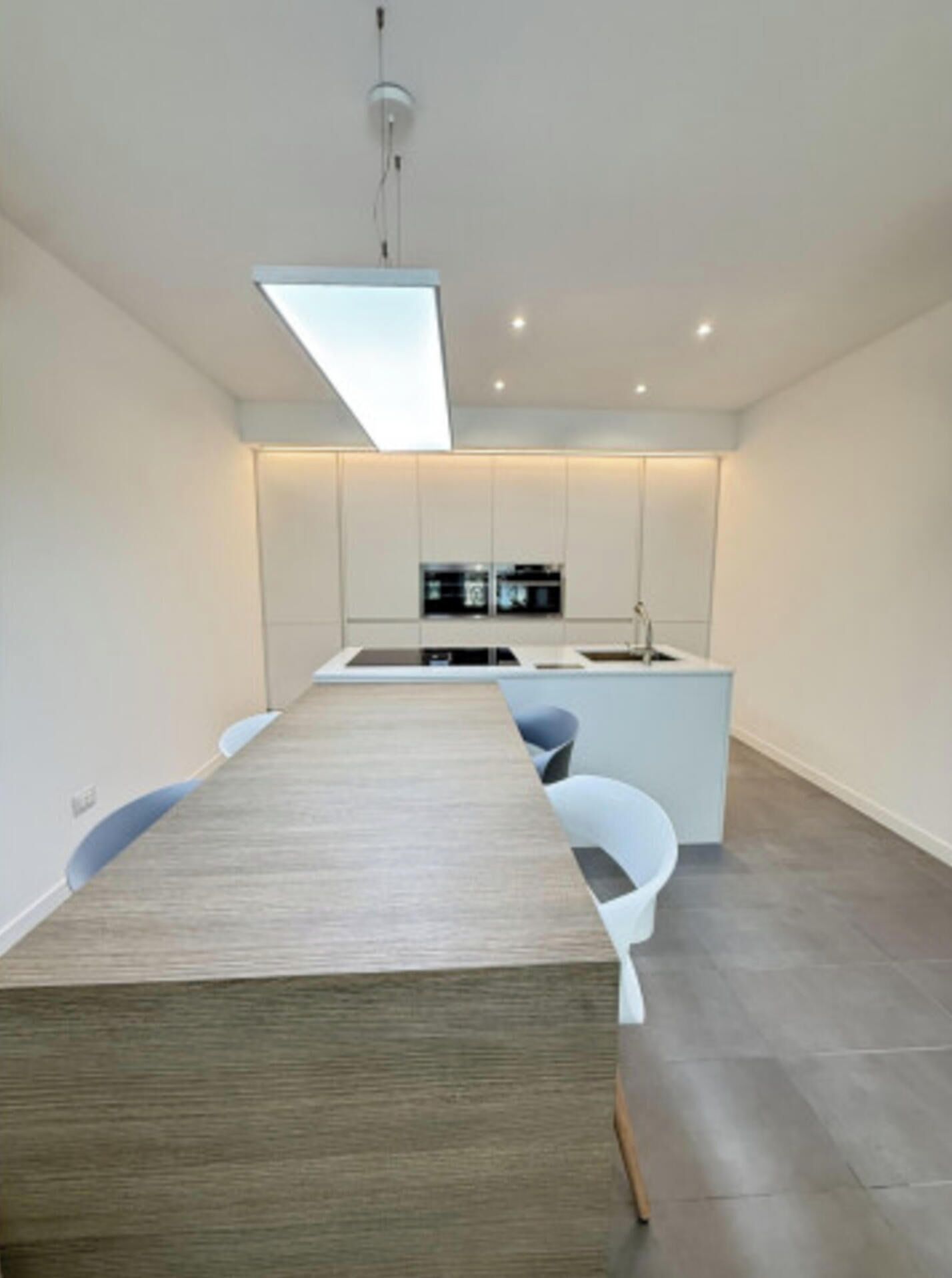 A modern kitchen with a central island, white cabinetry, and a long dining table.