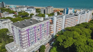 Un hotel a più piani con una facciata caratteristica nei toni del viola e del bianco, situato vicino a una spiaggia con vista libera sul mare.
